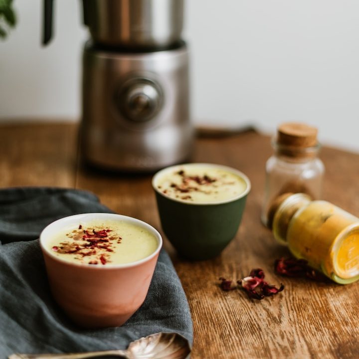 Warm cup of golden milk turmeric latte on a wooden table with cinnamon and ginger, promoting wellness and mindful living.